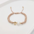 Detail of hand-woven bracelet with white pearl and gold letter T charm on tray - Letter I