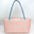 Close-up of pink quilted tote bag with floral patterns and blue contrast handles - Pink