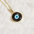 Bohemian gold evil eye pendant necklace with black enamel disc on white stone background - Black