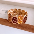 Dettaglio macro del bracciale elastico vintage dorato con logo G in smalto rosso e stelle - Oro-Giallo-Marrone