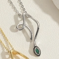 Macro della collana con ciondolo a orso e pietra marquise verde su sfondo in pietra bianca - Serpente/Curva Astratta / Argento