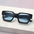 Close-up of modern thick-frame square sunglasses with light blue lenses on marble stand - Black Frame Blue Lens