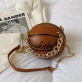 Brown basketball shaped crossbody bag with gold chain strap on soft white bedding - Brown