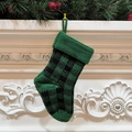 Calza di Natale in maglia a scacchi verdi e neri appesa a un camino bianco decorativo - Quadri Neri e Verdi