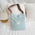 Close-up of blue and white striped canvas tote bag with brown shoulder strap on a cozy sofa - Contrast Color Shoulder Bag