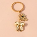 Elegante portachiavi a fiocco dorato con perle e strass su uno sfondo beige minimalista - Fiocco