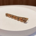 Close-up of golden metal hair clip with sparkling amber faceted crystals on white base - Round Champagne