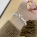 Elegant white pearl bracelet featuring a silver bow pendant on a female model's wrist - Silver Bow Pearl Beaded (MY37399)