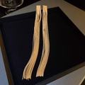 Detailaufnahme langer vergoldeter Quastenohrringe mit Dreiecksstecker auf schwarzem Samt - Gold