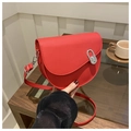 Close-up of red saddle bag with silver oval lock held by a model in a cafe setting - Red