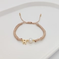Detailed macro view of handmade braided gold rope bracelet with letter R and pearl charm - Letter R