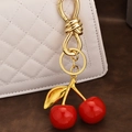 Golden keychain with shiny red resin cherry pendants hanging on a white quilted handbag - Light Gold Cherry Pendant