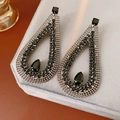 Dettaglio degli orecchini con zircone nero a goccia su un supporto in velluto grigio - Nero