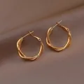 Détail de créoles dorées torsadées montrant le design tressé sur un tissu marron - 6# Tige d'Oreille en Argent - Tressé à Trois Brins