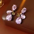 Dettaglio di orecchini vintage dorati con cristalli viola a goccia su pelle marrone - Viola