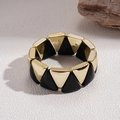 Nahaufnahme eines geometrischen Armbands mit Goldmetall und schwarzen Dreiecken auf einem Naturstein - Gold mit Schwarz