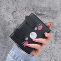 Short black bifold wallet featuring a cute cartoon cat face pattern held in hand - Black