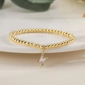 Bracelet à perles doré 18 carats avec pendentif éclair blanc posé sur assiette blanche - Pendentif Éclair (31921)