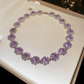 Vista macro di un pendente a fiore viola con diamanti in una scatola per gioielli - Collana Di Fiori Con Strass Viola / Viola