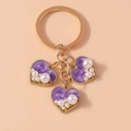 Detailed close-up of golden heart keychain with purple base and white inlaid pearls - Purple