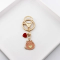 Détail d'un porte-clés chat en émail orange avec breloques cœur sur plateau blanc - Chat à Fermoir Mousqueton Rose