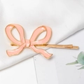 Elegante pasador dorado con lazo de esmalte rosa sobre una suave textura de seda blanca - Rosa