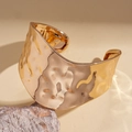 Detalle de brazalete ancho dorado con borde ondulado irregular y textura de metal martillado - Dorado