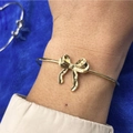 Dettaglio ravvicinato di un bracciale a polsino dorato con fiocco indossato su sfondo blu - Oro