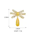 Detailansicht einer goldenen Schleifennadel mit Zirkonia und gelbem birnenförmigem Stein - B740 Goldgelb/Schleife