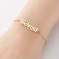 Vista macro de una pulsera dorada Babygirl con letra gótica en la muñeca de modelo - Dorado