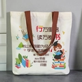 White canvas tote bag with brown handles and motivational cartoon illustrations - Travel and Read Widely