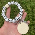 Detail eines Schlüsselanhängers mit Fußballperlen und Holzscheibe vor grünem Rasenhintergrund - Schwarz & Weißer Fußball-Stil
