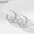 Sleek silver bamboo textured C-shaped hoop earrings on white stone background - 18K Purity / Steel