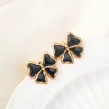 Detailed view of golden bow earrings with black enamel inlay on a white ceramic edge - Black
