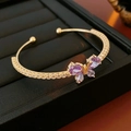 Close-up of golden butterfly bracelet with purple zircon stones on black leather - Gold-Purple