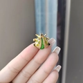 Golden beetle brooch with sparkling green gemstone inlay held for size display - Green