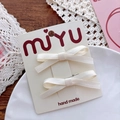 Detail of cream handmade bow hair clips displayed on a branded card over a rustic table - Off-white