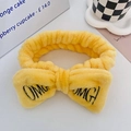 Yellow plush headband with large bow and black OMG embroidery on white surface - Yellow