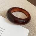Detail of amber resin bangle showing marbled texture on beige textured fabric surface - Shaded Amber (Brown-Ink Round)
