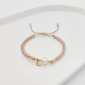 Macro detail of hand-woven cord bracelet featuring a natural pearl and golden letter L charm - Letter L