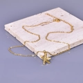 Detail view of gold starfish pendant necklace on textured white stone surface - Starfish