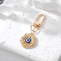 Close-up of golden flower keychain with blue evil eye bead on white stone - 7# Blue Pink Eye Flower