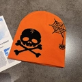 Close-up of orange knit beanie with black skull and spider web patterns on stone background - M (55-59cm) / Orange