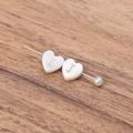 Natural shell heart bead with golden letter J and pearl accent on wooden background - Letter J