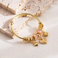 Détail de breloques en cœur doré et perles de verre sur un bracelet jonc torsadé doré - Rose