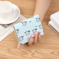 Short light blue trifold wallet featuring cartoon cow prints on a rustic wooden desk - Cute Cow Blue