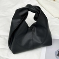 Borsa hobo nera minimalista con manico annodato esposta su un panno bianco morbido - Nero