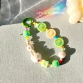 Détail macro d'une chaîne perlée colorée avec poupée, boule peluche et lumière arc-en-ciel - Vert