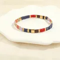 Detail of colorful Tila bead stretch bracelet with enamel tiles in a shell tray - Navy Red Chocolate Purple Pink Gold