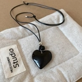 Detail shot of a black heart pendant necklace with polished resin on a white quilted pouch - 25# Necklace-Black